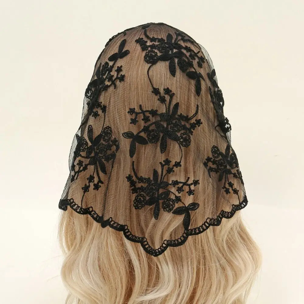 Black floral lace triangle headscarf draped over blonde hair against a pale background. The open floral pattern and scalloped border stand out clearly over the lighter hair.
