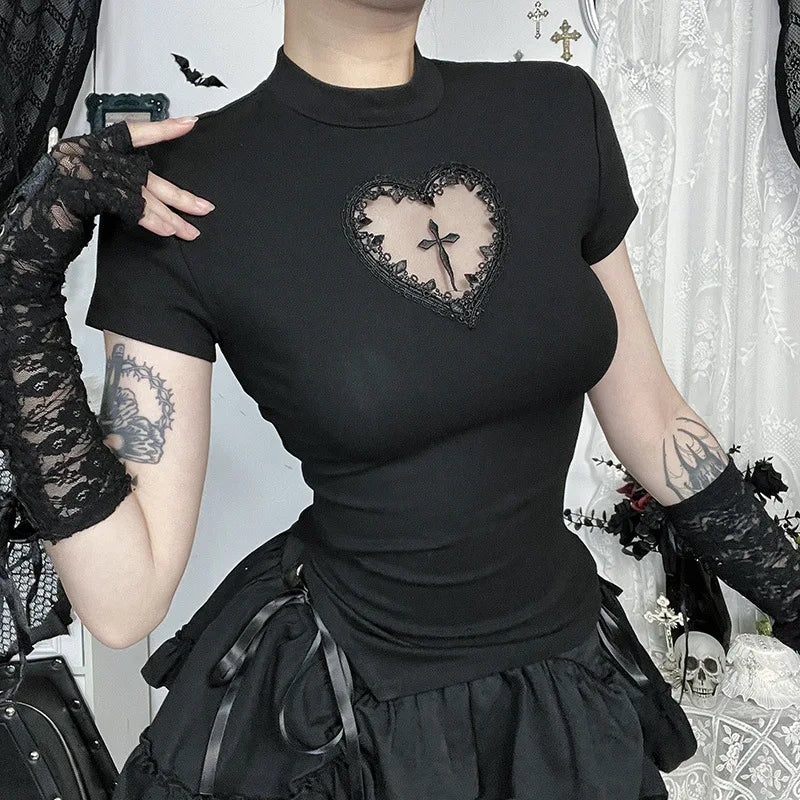Black T-shirt worn with a hand near the shoulder, showing the lace-edged heart and cross detail against a gothic room setting.