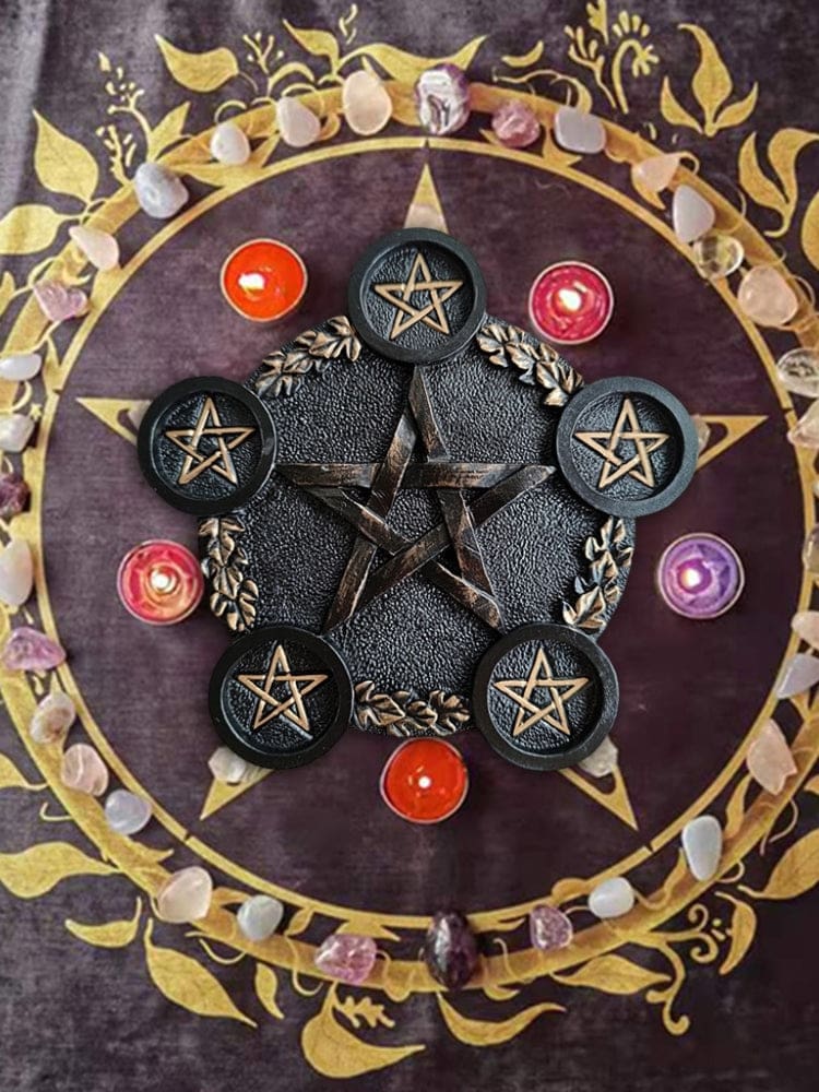 Black pentagram candle holder on a patterned altar cloth, with five round platforms, leaf details and small candles arranged around it.