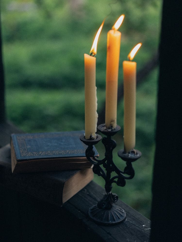 Three yellow ritual candles standing on a wooden outdoor surface, showing their slender shape and exposed wicks.