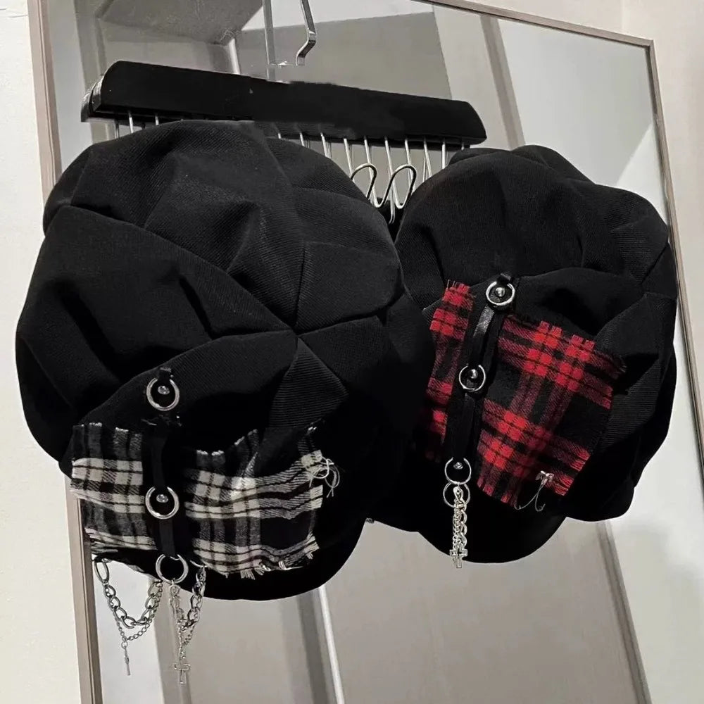 Top view of two black punk newsboy caps showing paneled crowns, frayed plaid patches and metal ring accents.