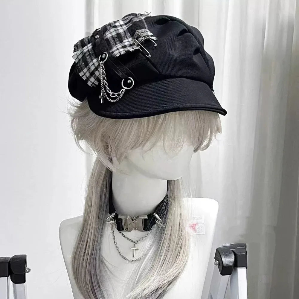 Black gothic newsboy cap with a monochrome plaid patch, safety-pin accents, draped chains and a curved brim.