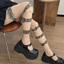 Seated view of beige gothic tights with buckle and eyelet prints, styled with black platform Mary Jane shoes.