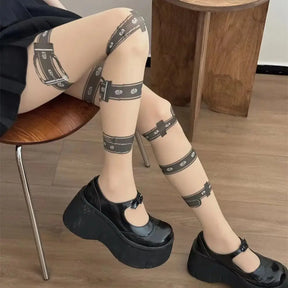 Seated view of beige gothic tights with buckle and eyelet prints, styled with black platform Mary Jane shoes.