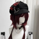Red plaid gothic newsboy cap on a mannequin, showing its curved brim, decorative chains and dangling cross charm.