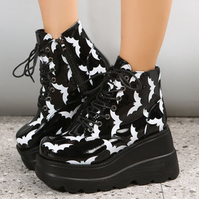 Side view of black bat-print platform boots, showing the ankle zippers, white bat silhouettes and deep ridges along the soles.
