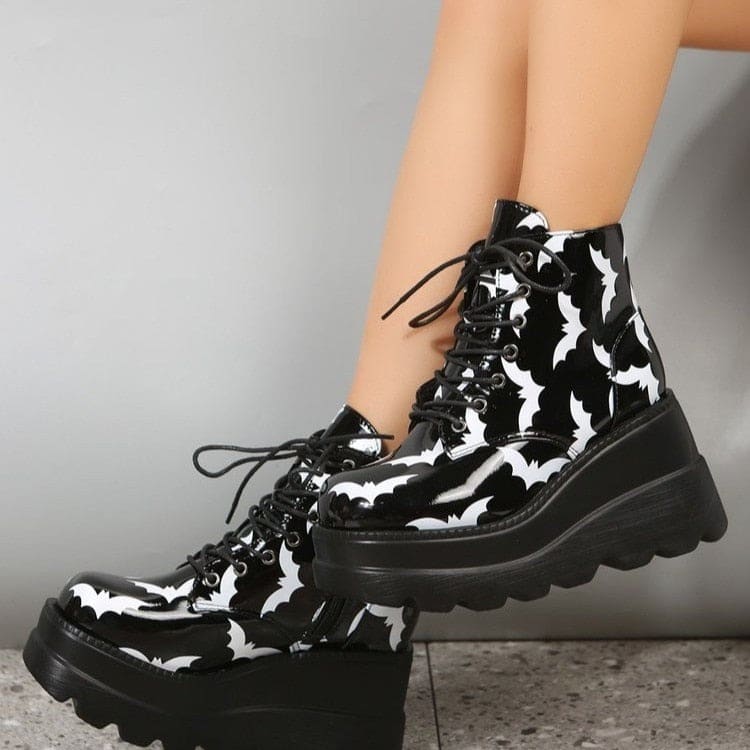Bat-print platform boots worn with crossed ankles, showing the glossy side panels and the height of the wedge-shaped soles.