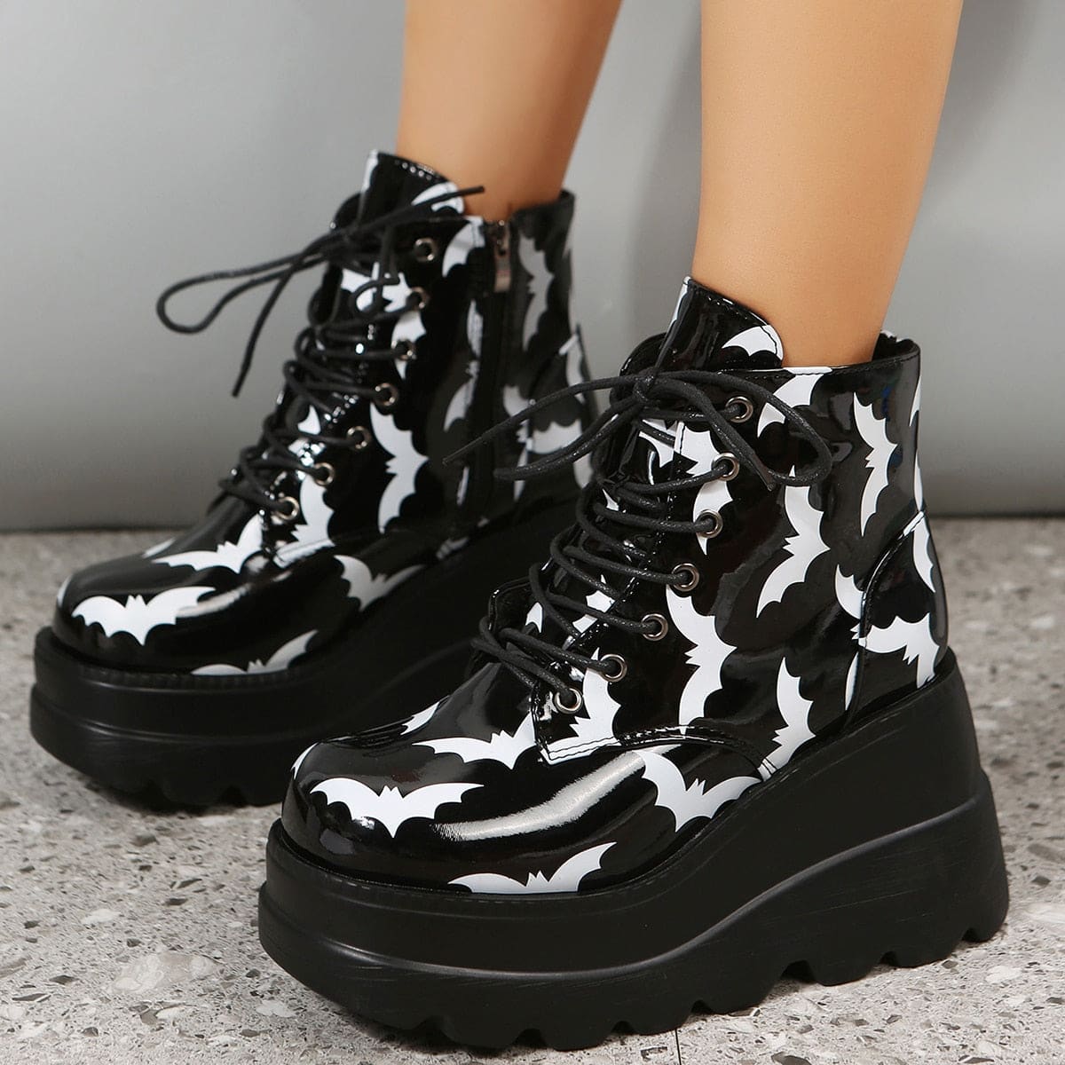 Pair of black-and-white bat-print ankle boots viewed from the front at an angle, showing laces, silver-tone eyelets and chunky wedge-shaped soles.