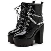 Pair of glossy black platform ankle boots on white, with lace-up fronts, silver-tone draped chains and tall block heels.