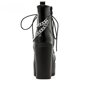 Rear view of a glossy black platform boot on white, showing the tall block heel, pull tab and silver-tone chains around the ankle.