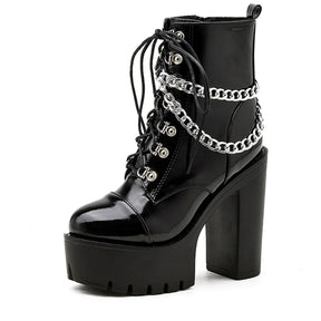 Single glossy black platform ankle boot angled on white, showing its front laces, draped silver-tone chains and tall block heel.
