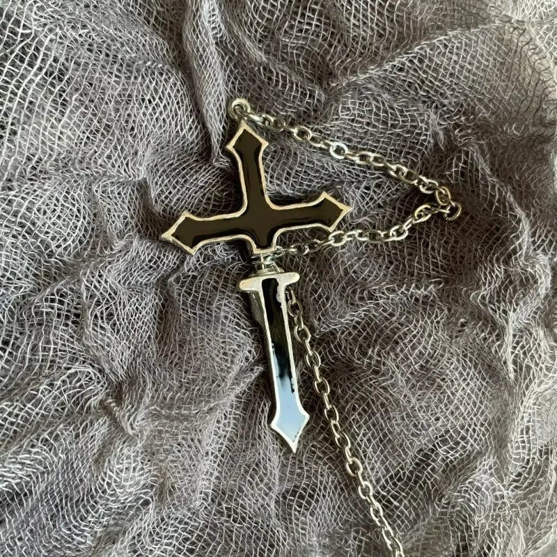 Black split cross earring resting on loosely woven gray fabric, with its chain curled around the two cross sections.