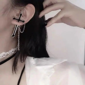 Black split cross earring worn with a white blouse and dark choker. The upper and lower cross sections sit on either side of the earlobe with chains hanging below.