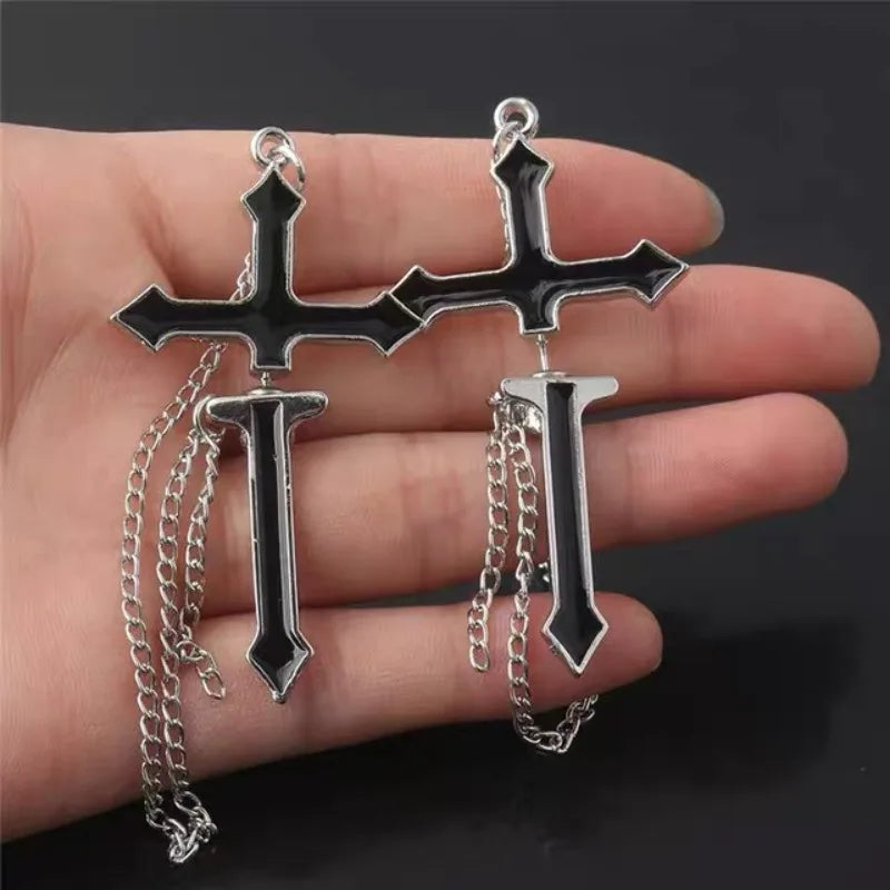 Pair of black split cross earrings held across a hand, showing the pointed lower sections and long silver-tone chain loops.