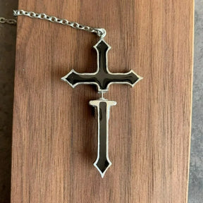 Black split cross chain earring laid flat on wood, with its two sections aligned to show the complete cross shape and gap between them.