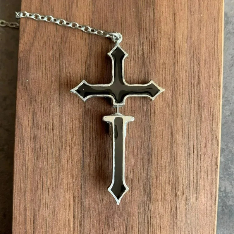 Black split cross chain earring laid flat on wood, with its two sections aligned to show the complete cross shape and gap between them.