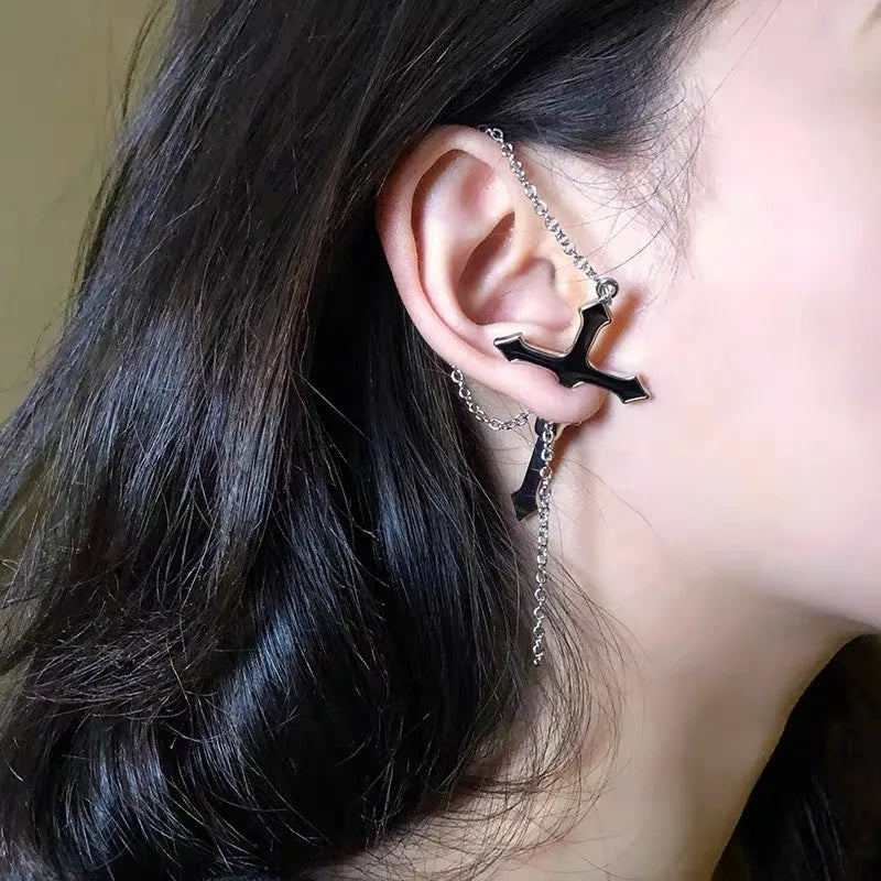 Black split cross earring worn outdoors with the fine upper chain draped over the ear. The lower cross and hanging chain stand out beside dark hair.
