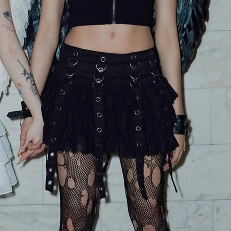 Front model view of the black gothic skirt, with hands beside the hanging eyelet straps and patterned tights visible below the ruffled hem.