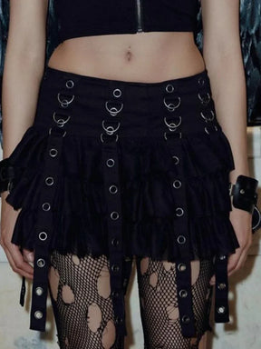 Front portrait crop of a model wearing the black eyelet strap skirt with a zip-front crop top and patterned tights; the straps extend below the ruffled hem.