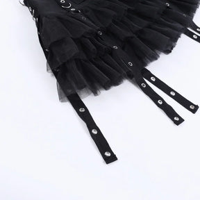 Close view of the black skirt's mesh ruffles and long flat straps with silver-tone eyelets on a white surface.