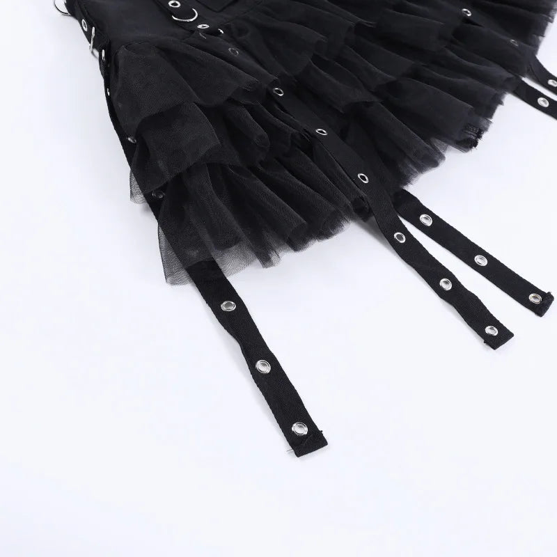 Close view of the black skirt's mesh ruffles and long flat straps with silver-tone eyelets on a white surface.