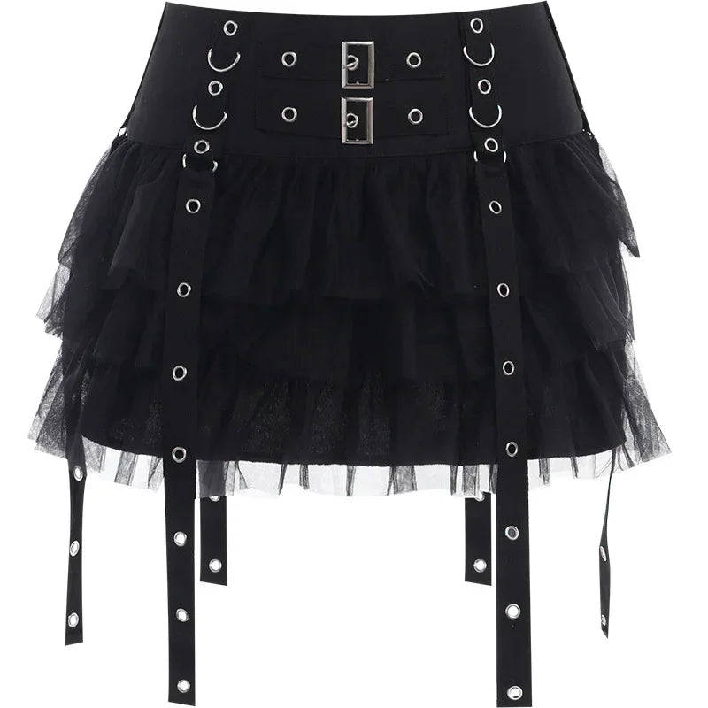 Black eyelet strap mini skirt isolated on white, showing two rectangular front buckles, rows of rings and layered mesh ruffles.