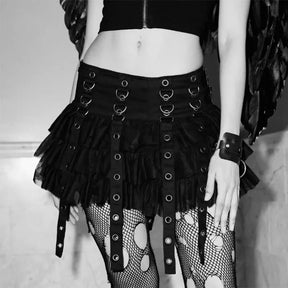 Black ruffle mini skirt in a monochrome outfit photograph, with rows of silver-tone rings and long eyelet straps layered over torn-pattern tights.