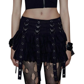 Model wearing the black eyelet strap skirt and patterned tights against white, showing the front rings and layered mini hem.
