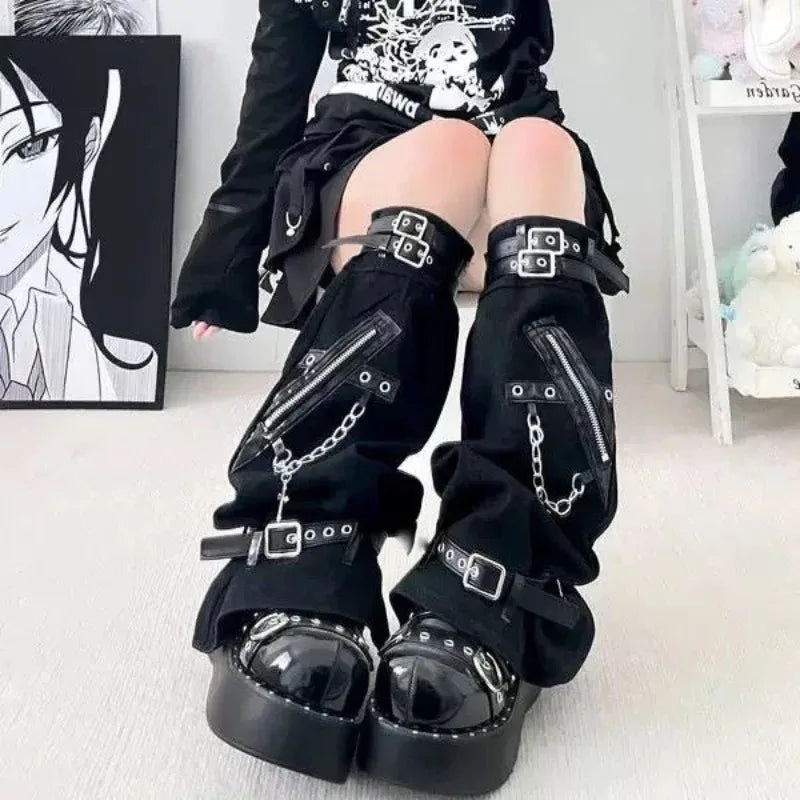 Close front view of black gothic leg warmers with buckle straps, diagonal zippers, chains and flared openings over platform shoes.