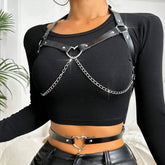 Black heart ring chain harness worn over a fitted black long sleeve crop top, with the matching slim heart belt around the bare waist above black trousers.