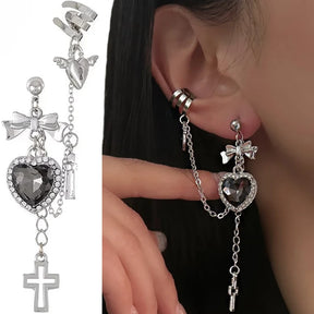 Black heart earring and chain cuff shown against white beside a model wearing the design. The heart has a sparkling border, with a bow above and a cross drop below.