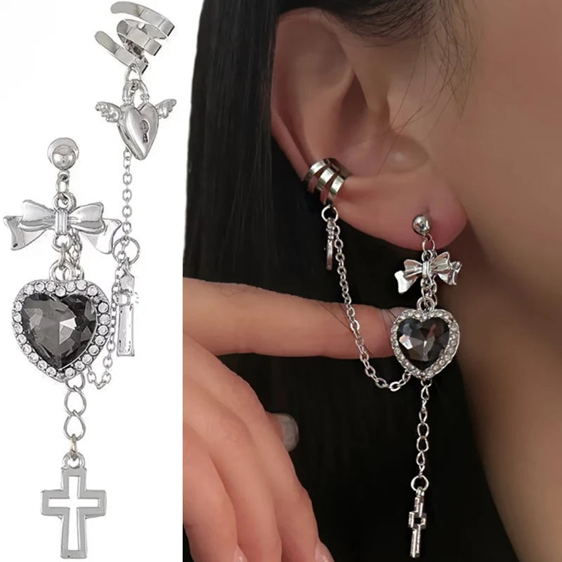 Black heart earring and chain cuff shown against white beside a model wearing the design. The heart has a sparkling border, with a bow above and a cross drop below.