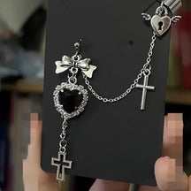 Black faceted heart and bow chain earring displayed on a dark card, with a winged heart upper cuff and two hanging cross charms.