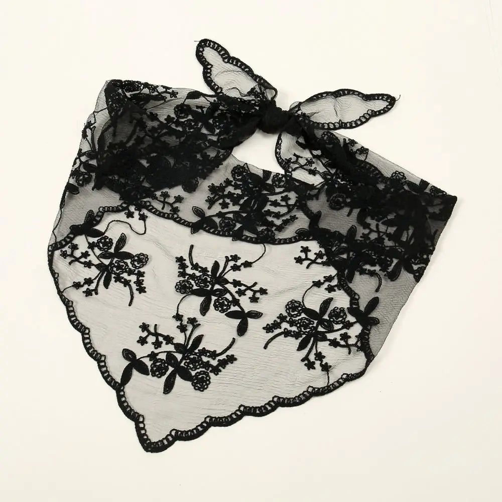 Black floral lace bandana tied and laid flat on a pale background. Fine netting, embroidered-looking flowers and the scalloped triangular border are visible in close detail.