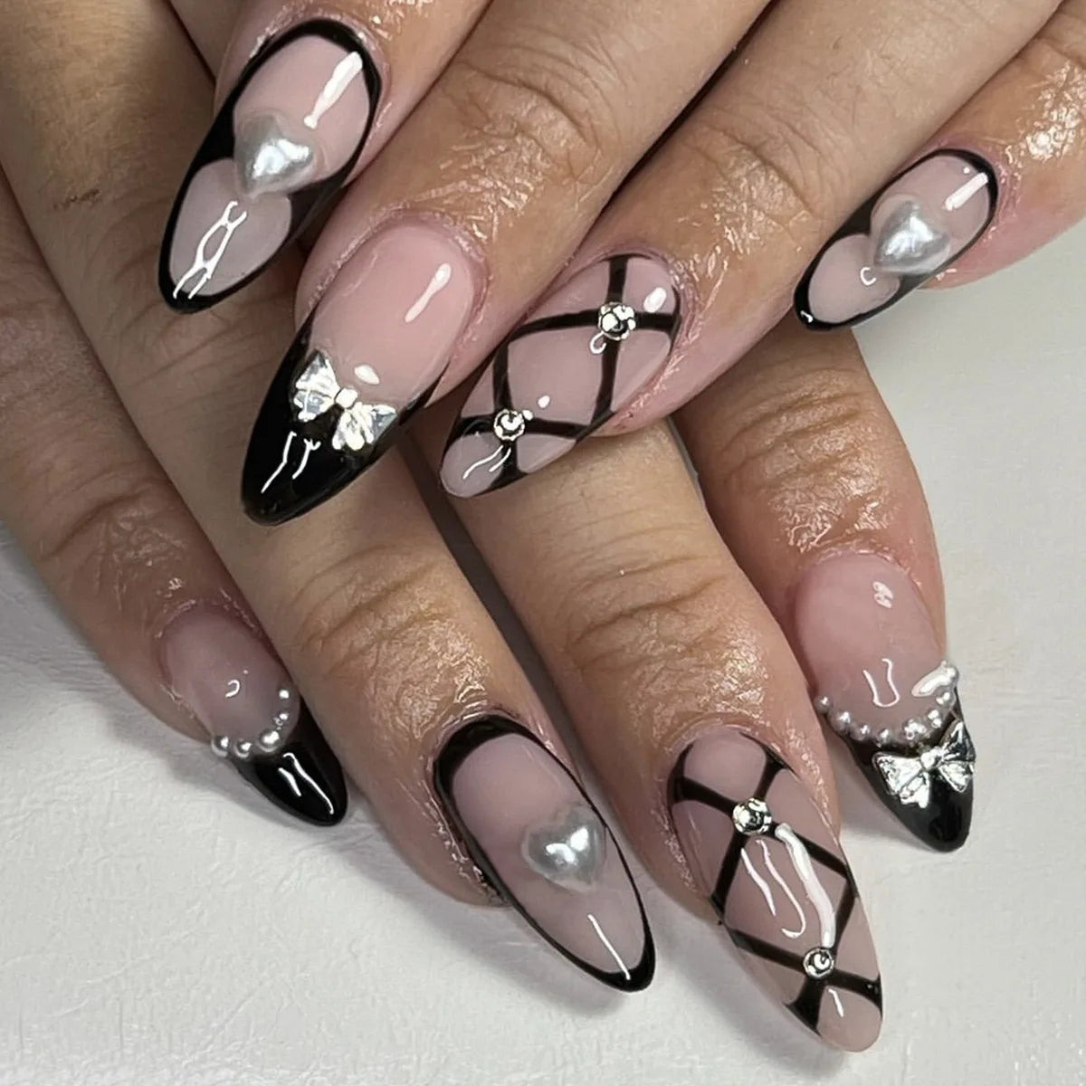 Alternate nail design reference showing nude nails with thin black outlines, heart-shaped pearl-like accents and crossed black lines.
