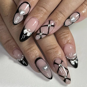 Alternate nail design reference showing nude nails with thin black outlines, heart-shaped pearl-like accents and crossed black lines.