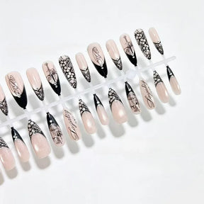 Two rows of black-and-nude nail tips on white, displaying lace panels, script and slender gothic artwork.