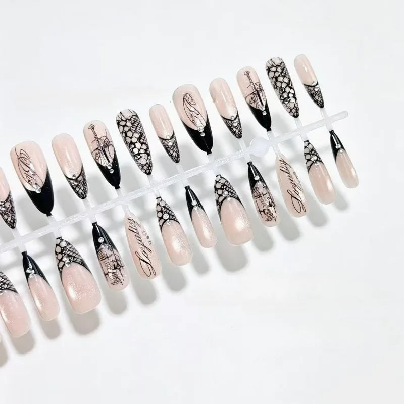 Two rows of black-and-nude nail tips on white, displaying lace panels, script and slender gothic artwork.