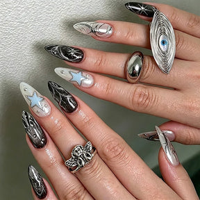 Alternate nail design reference with black and silver-tone star artwork, shown on hands wearing statement rings against a pale textured background.