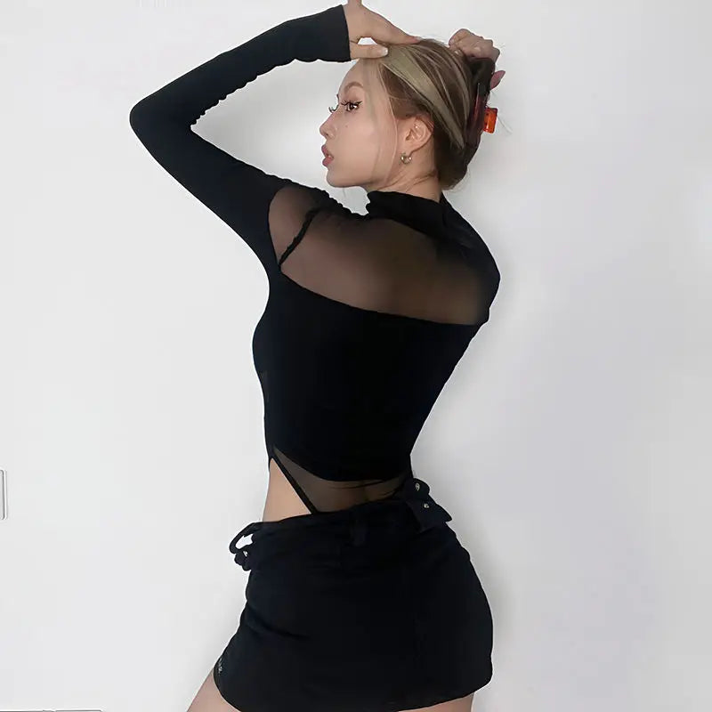 Rear three-quarter view of the black long sleeve bodysuit, with a sheer upper-back panel above an opaque middle section and mesh at the waist.