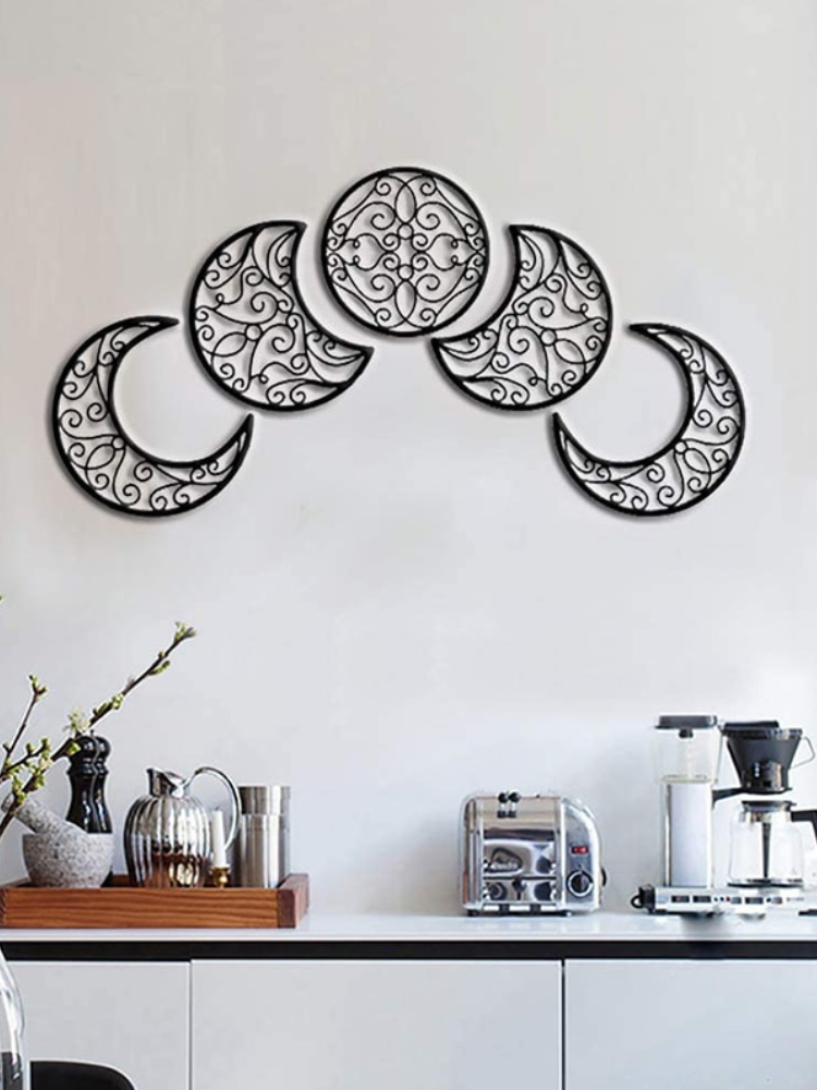 Black scrollwork moon-phase wall art arranged in a curved row over a sideboard with plants and kitchen accessories.