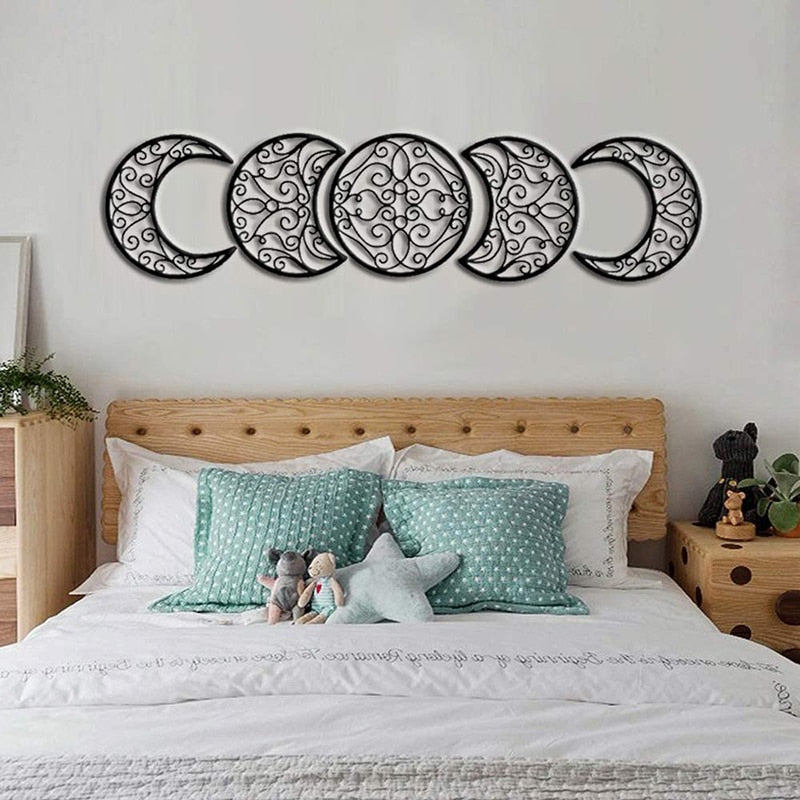 Five black scrollwork moon cutouts arranged in a straight row above a wooden bed frame and pale bedding.