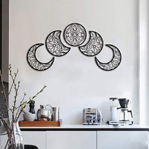 Five black wooden lunar shapes on a pale wall, with the full moon raised above the crescents in a balanced arc.