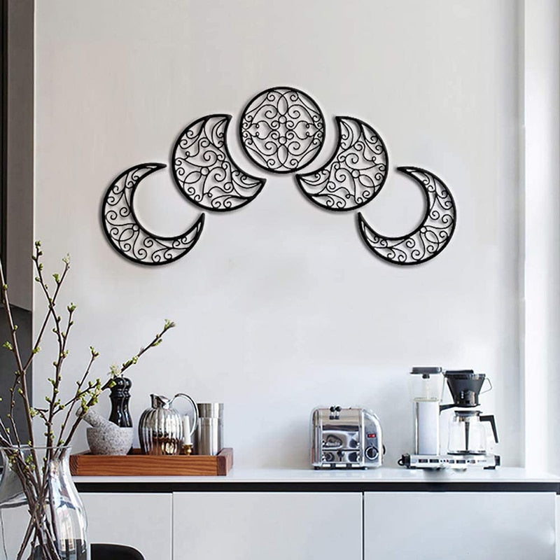 Five black wooden lunar shapes on a pale wall, with the full moon raised above the crescents in a balanced arc.