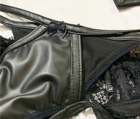 Close view of the black briefs, showing narrow crossing straps, a tiny bow and stitched glossy panels.