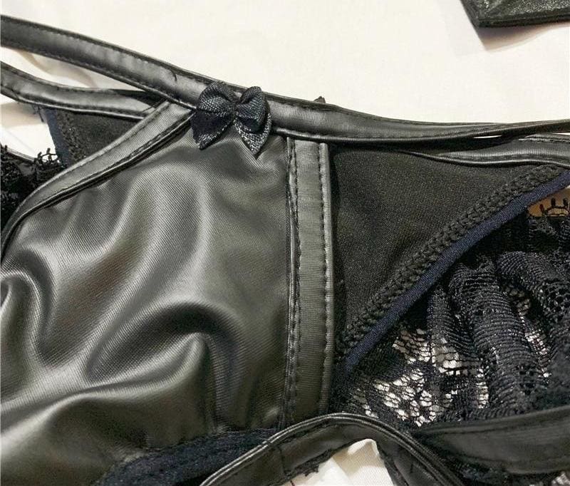 Close view of the black briefs, showing narrow crossing straps, a tiny bow and stitched glossy panels.