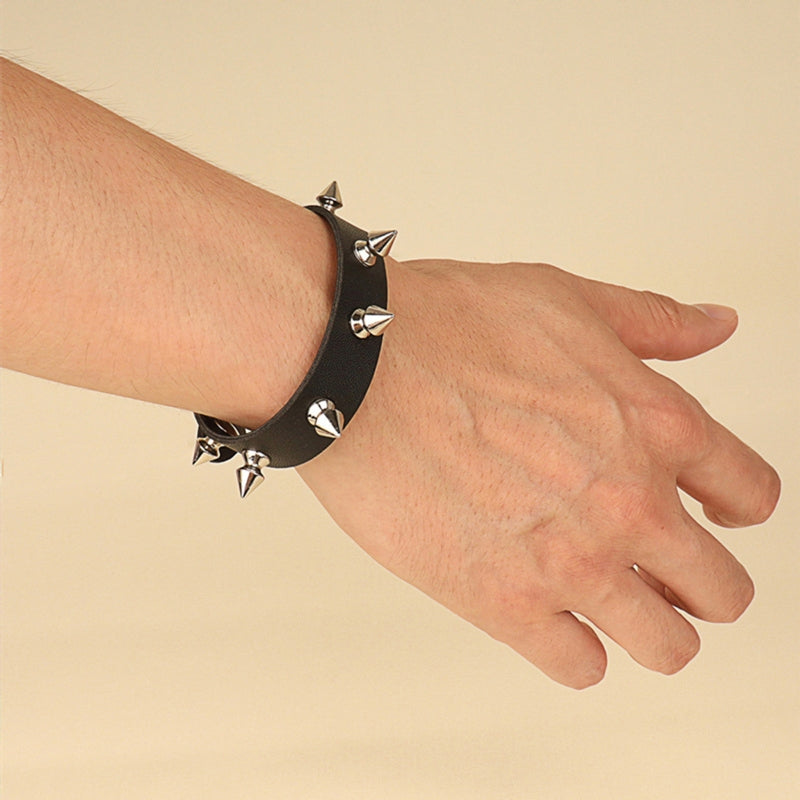 Narrow black bracelet worn on a wrist with one row of silver-tone pointed spikes against the plain black band.