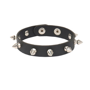 Narrow black cuff bracelet against white with a single row of silver-tone spikes and adjustable snap fastenings.