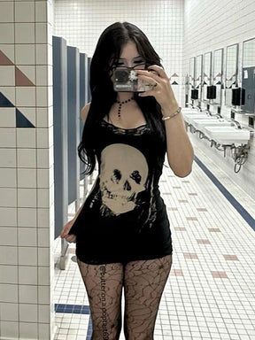 Portrait mirror photograph of the black skull mini dress worn with patterned tights in a tiled room.