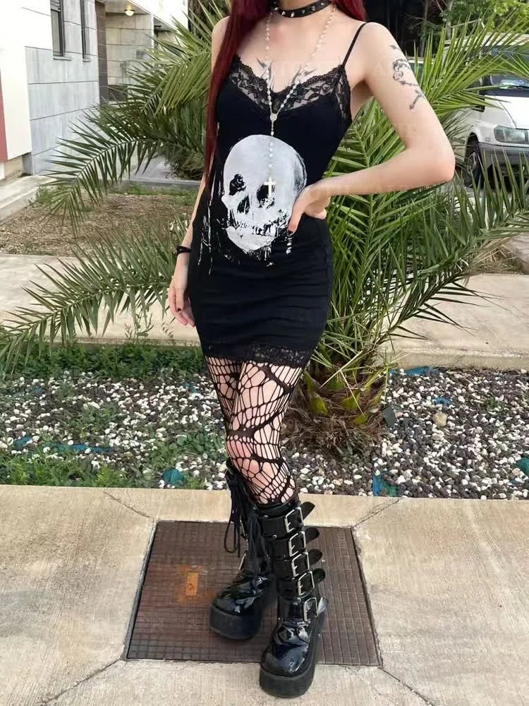 Full outdoor outfit view of the black skull lace mini dress styled with patterned tights and chunky boots beside garden plants.